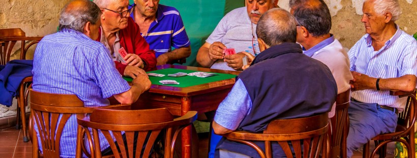 Several older men seated around a table playing cards