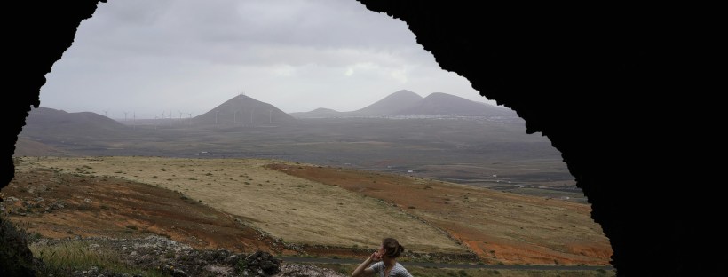 A landscape of brown hills and far off mountains framed by the entry of a cave