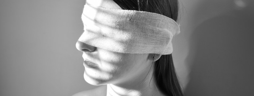 A young woman with a bandage around her eyes faces toward a sunlit window